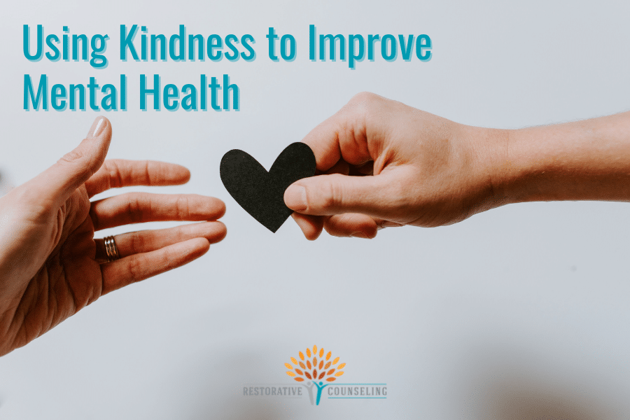 one hand holding a paper heart, offering it to another outstretched hand, showing the relationship between kindness and mental health. end id.